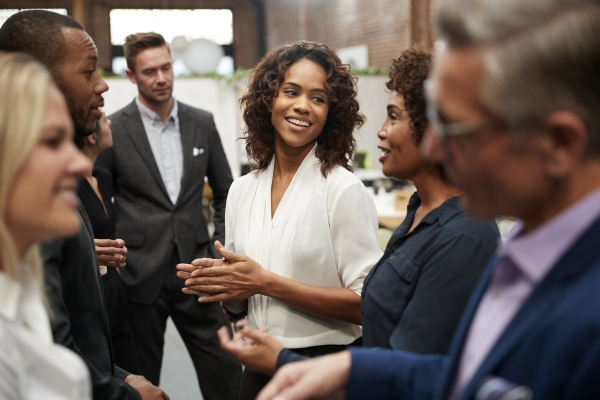 Seven business colleagues in good spirits chatting. In focus are two Black women, a Black man, two white men and a white woman